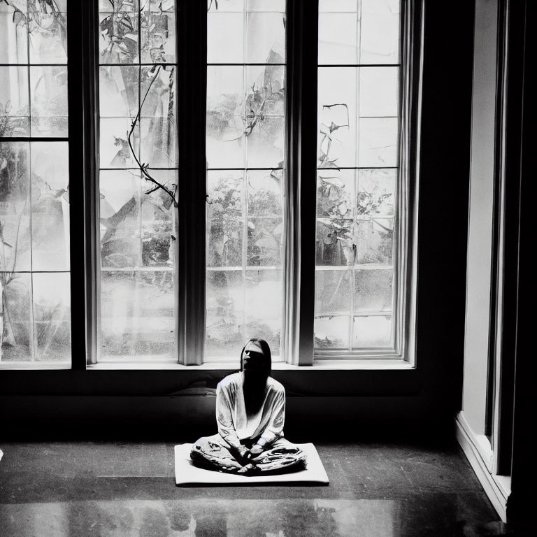 Individual in dimly lit room by large window with translucent curtains