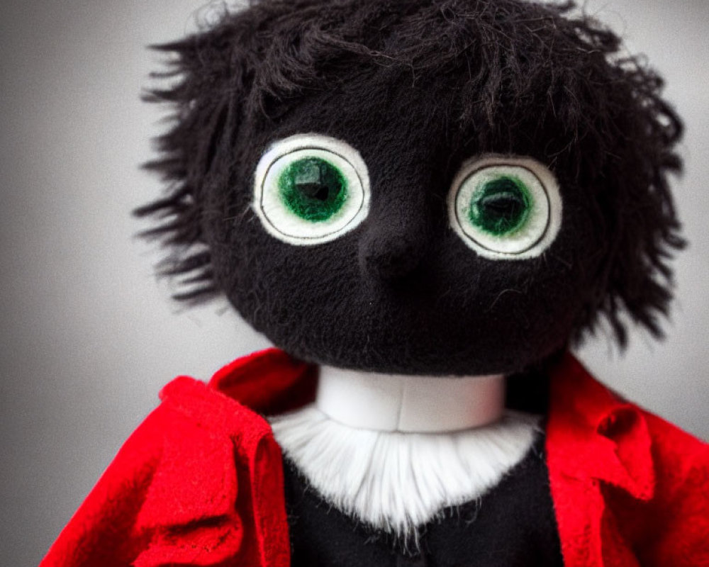 Plush Toy with Large Green Eyes and Red Cape on Grey Background