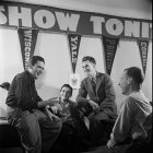 Four men laughing in front of backdrop with man in multiple poses