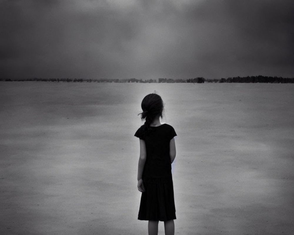 Lonely young girl in black dress in desolate landscape under cloudy sky