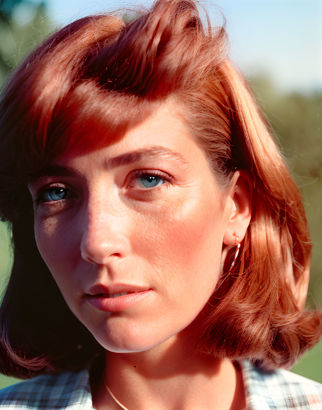 Portrait of person with short auburn hair and blue eyes wearing earring on green background