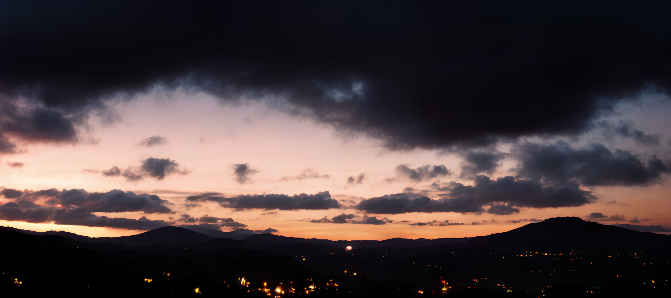 Scenic sunset panorama with silhouetted mountains and town lights