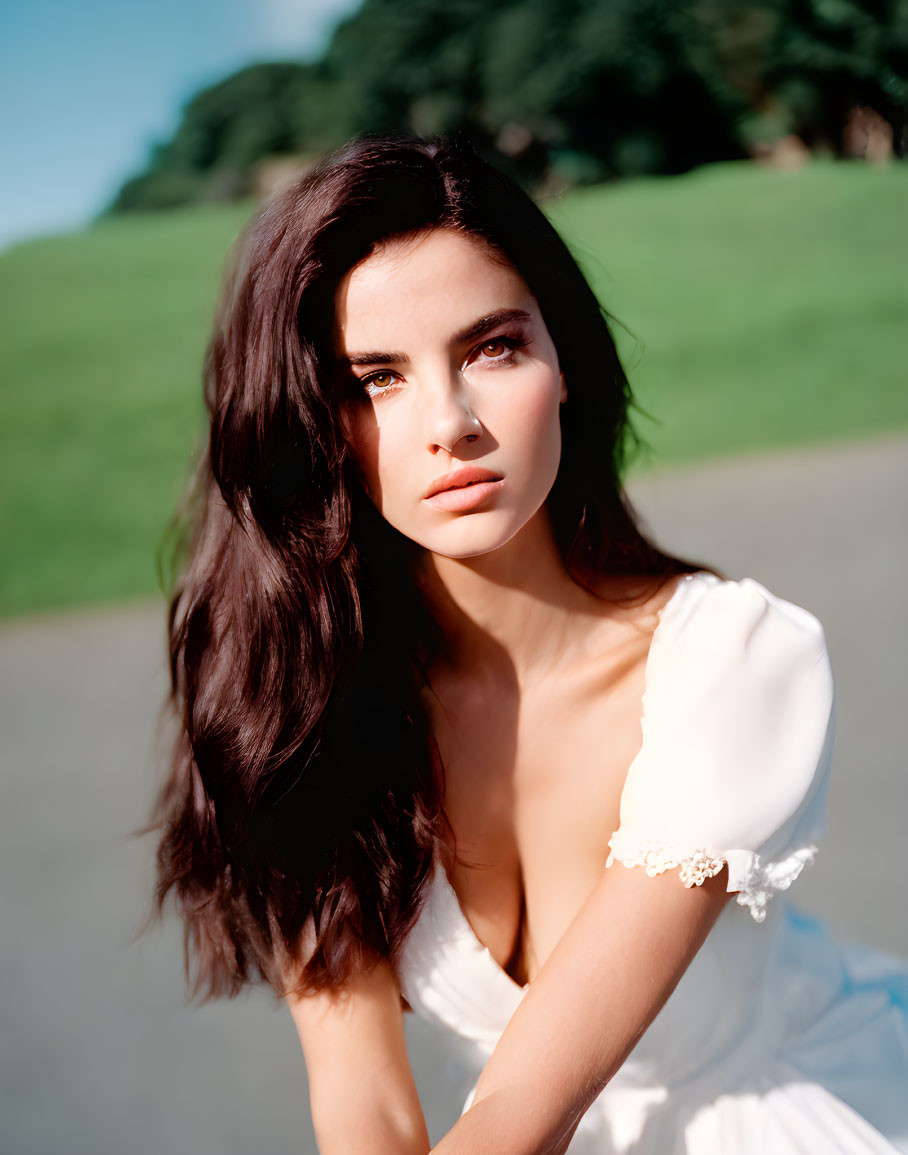 Dark-haired woman in white dress gazes against green backdrop