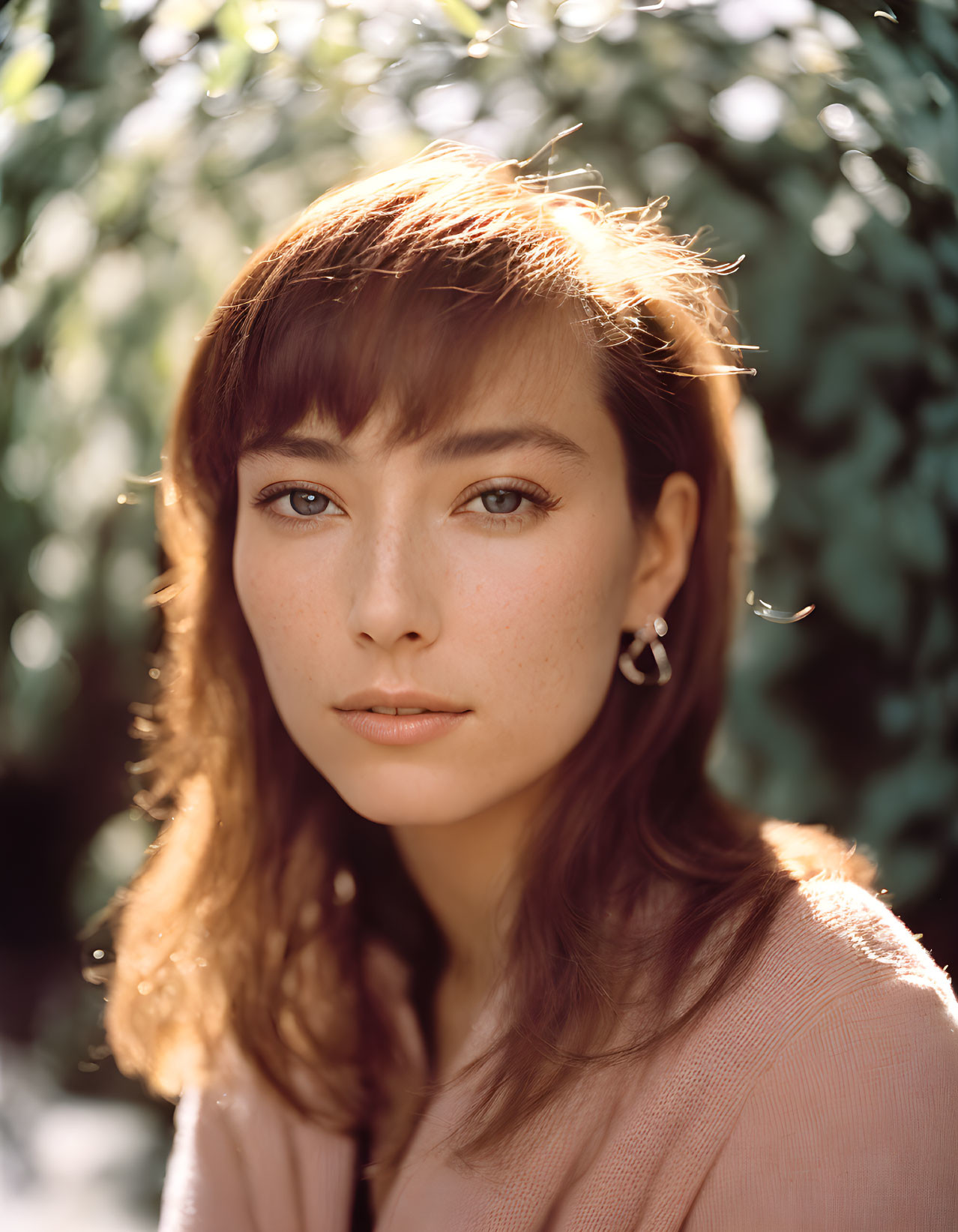 Portrait of woman with bangs, freckles, brown hair, pink top, hoop earrings,