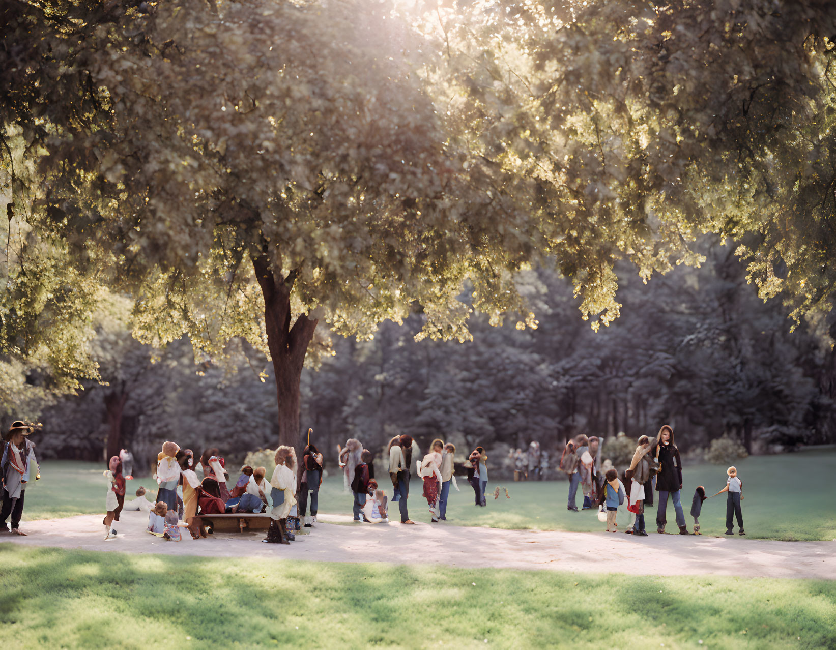 Sunny day in park with lush green trees, people sitting on benches or walking.