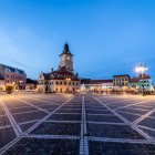 Traditional town square with cobblestones, buildings, and clock tower at dusk