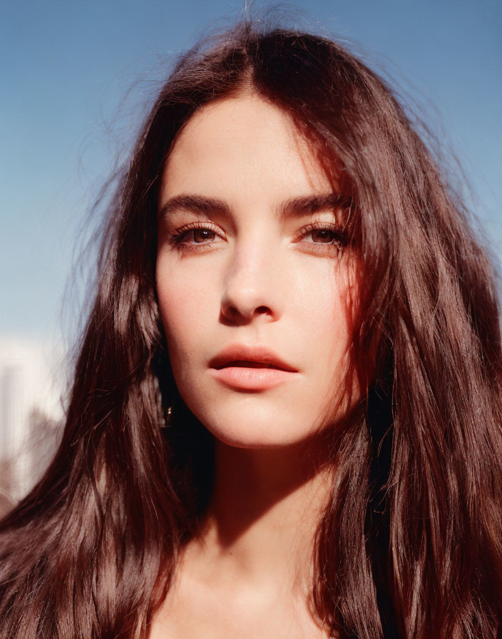 Portrait of woman with dark hair, fair skin, and light eyes against blue sky.