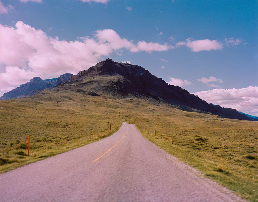 Scenic road leading to rugged mountains under blue sky