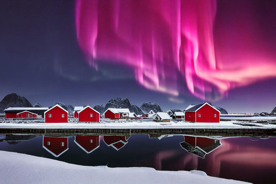 Snow-covered red wooden cabins by tranquil lake under purple night sky with vibrant aurora borealis