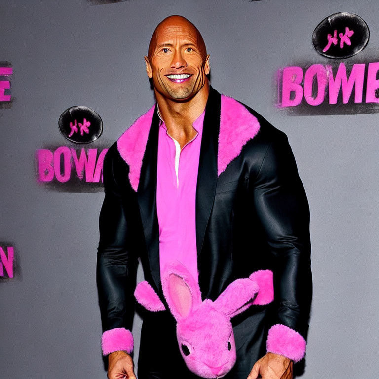 Muscular man in suit with pink fur trim holding bunny plush at promotional event