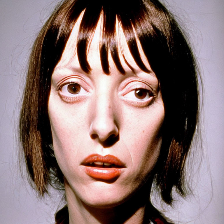 Portrait of woman with short brown hair and bangs, wearing noticeable makeup.