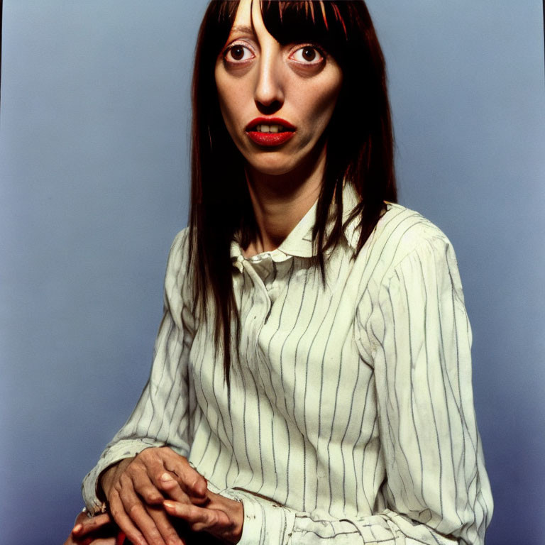 Portrait of Woman with Long Dark Hair and Red Lipstick in White Striped Shirt against Blue Background