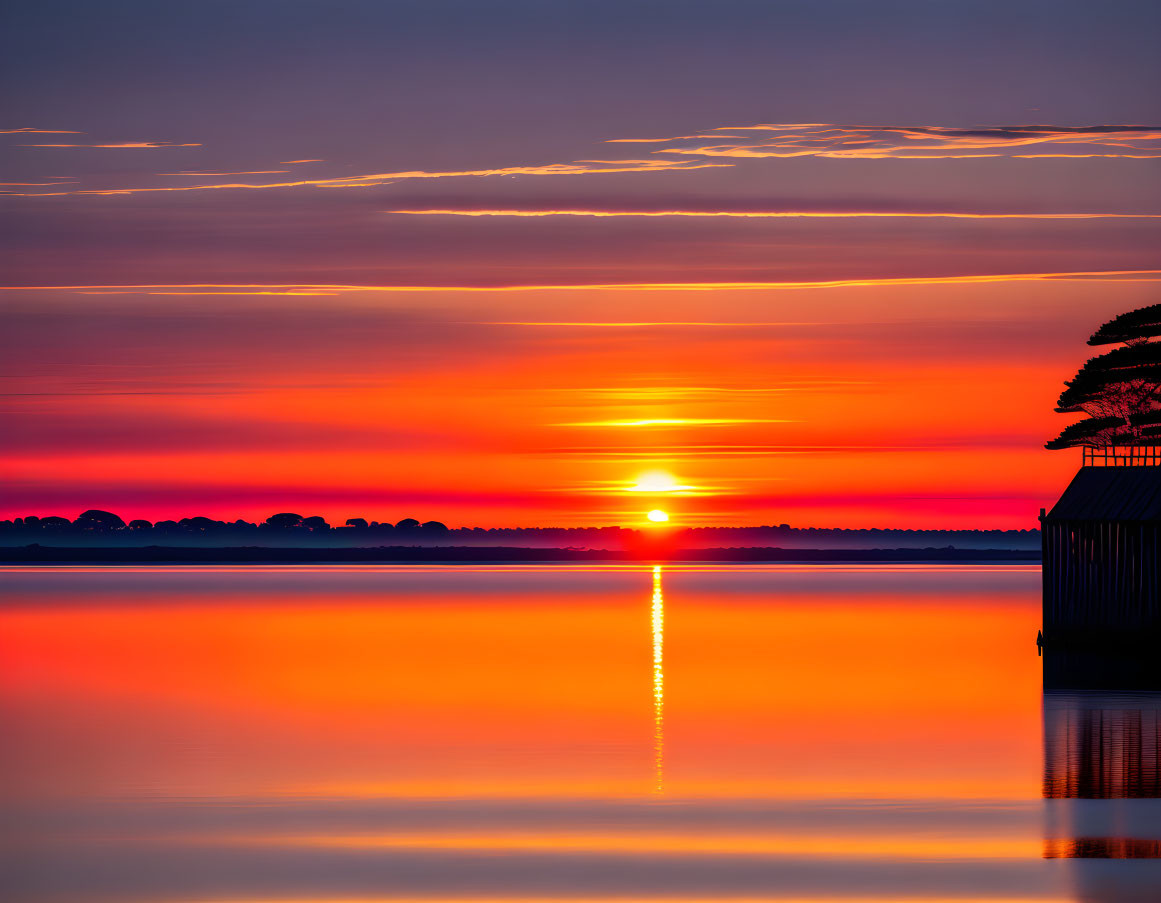 Scenic sunset over calm lake with orange reflections and silhouetted trees