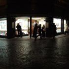 Night scene: Silhouettes passing by brightly lit store on cobblestone pavement