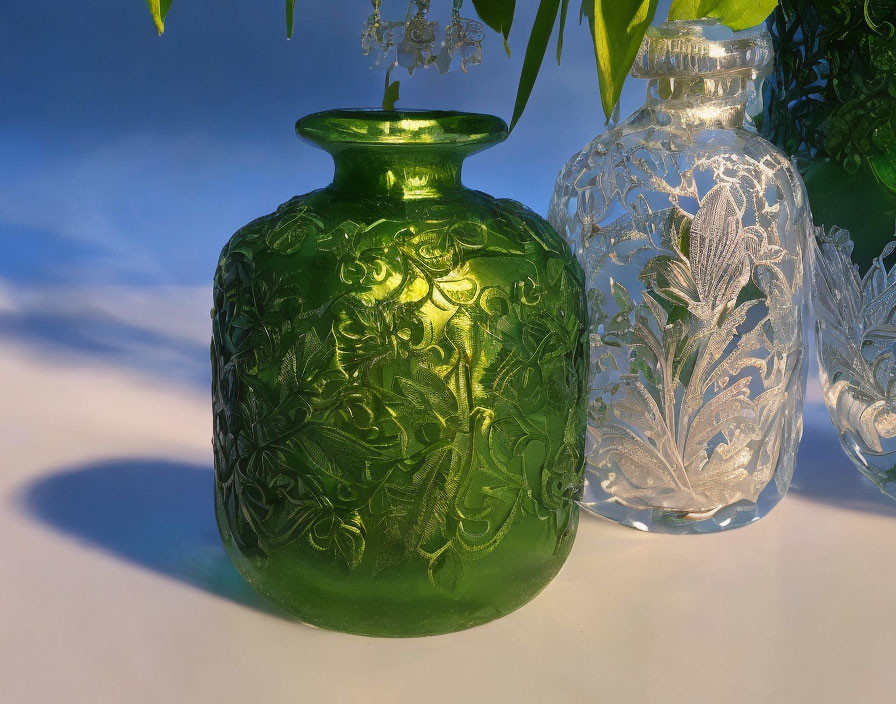 Ornate green and clear glass jars with embossed patterns on foliage backdrop