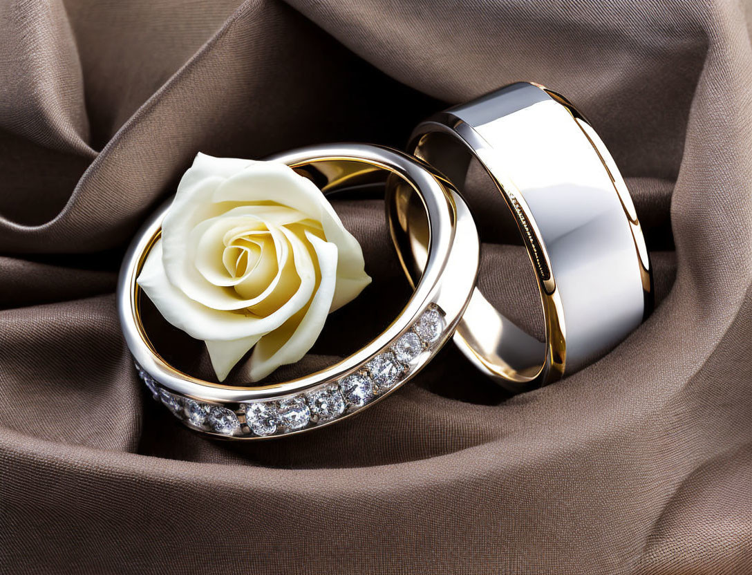 Diamond-encrusted wedding bands with white rose on brown silk fabric