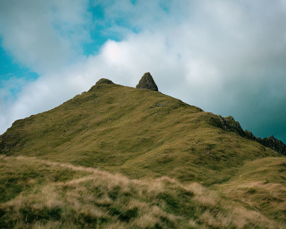 Grassy Hill and Rocky Peak under Cloudy Sky