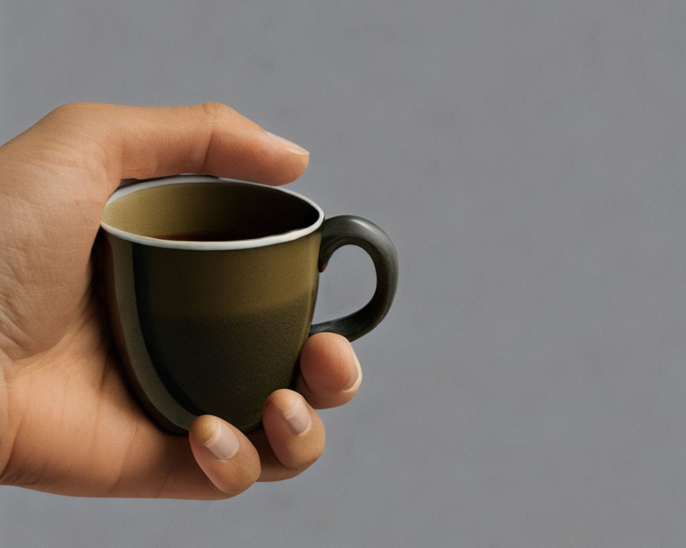 Dark-colored cup held by hand on grey background.