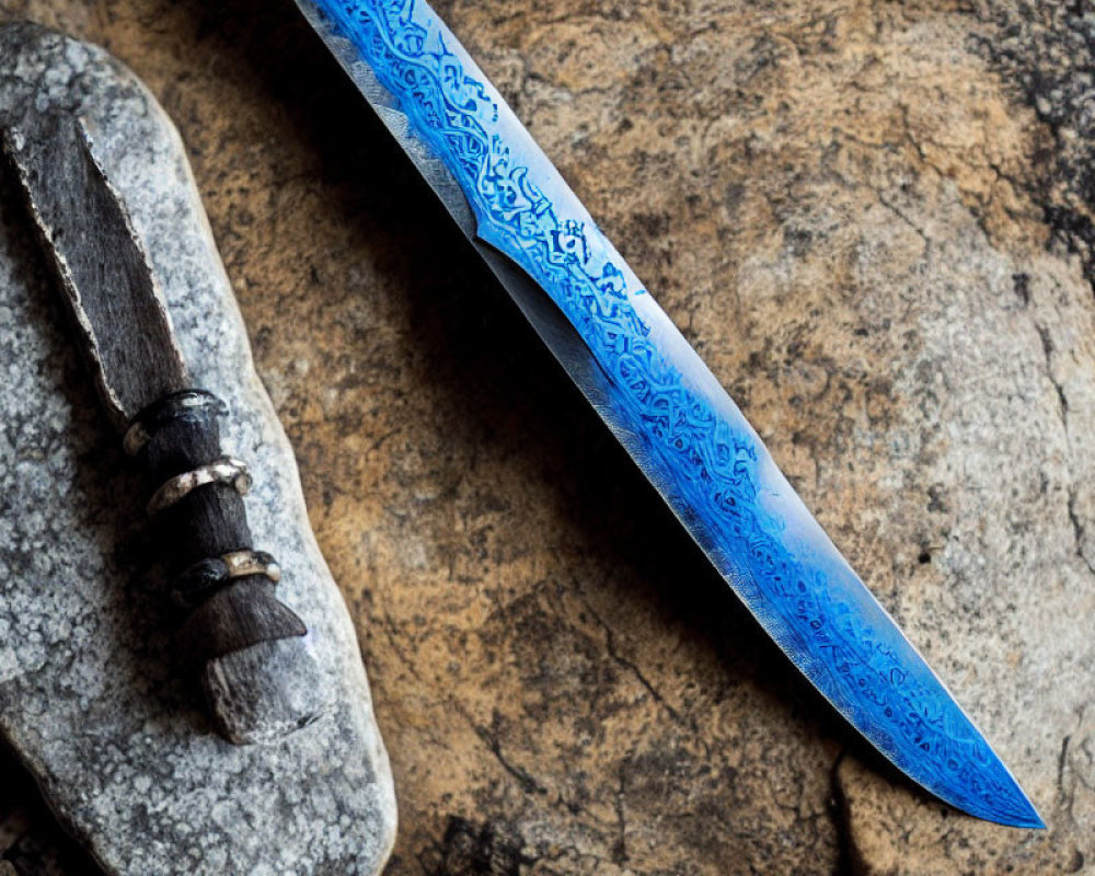 Patterned Blue Knife Blade Next to Primitive Stone Tool on Textured Rock Surface