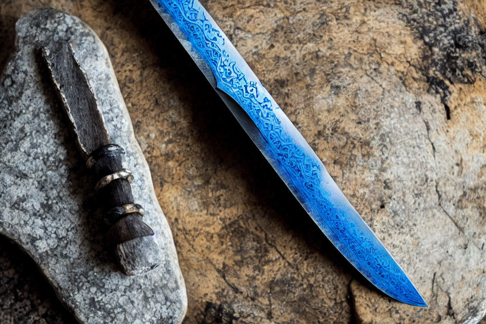 Patterned Blue Knife Blade Next to Primitive Stone Tool on Textured Rock Surface