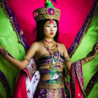 Elaborate traditional Asian attire with golden crown and jewelry on vibrant pink backdrop