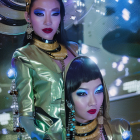 Futuristic women in metallic outfits with blue makeup and stylish hats surrounded by glowing lights