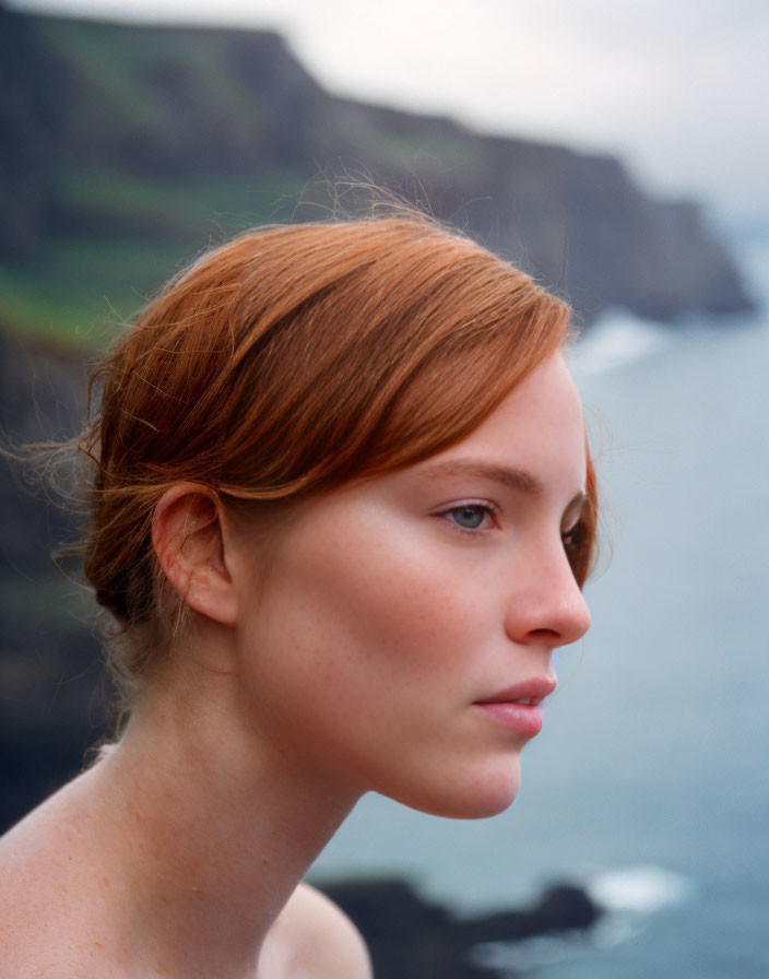 Red-haired woman gazes at coastal cliffs and ocean