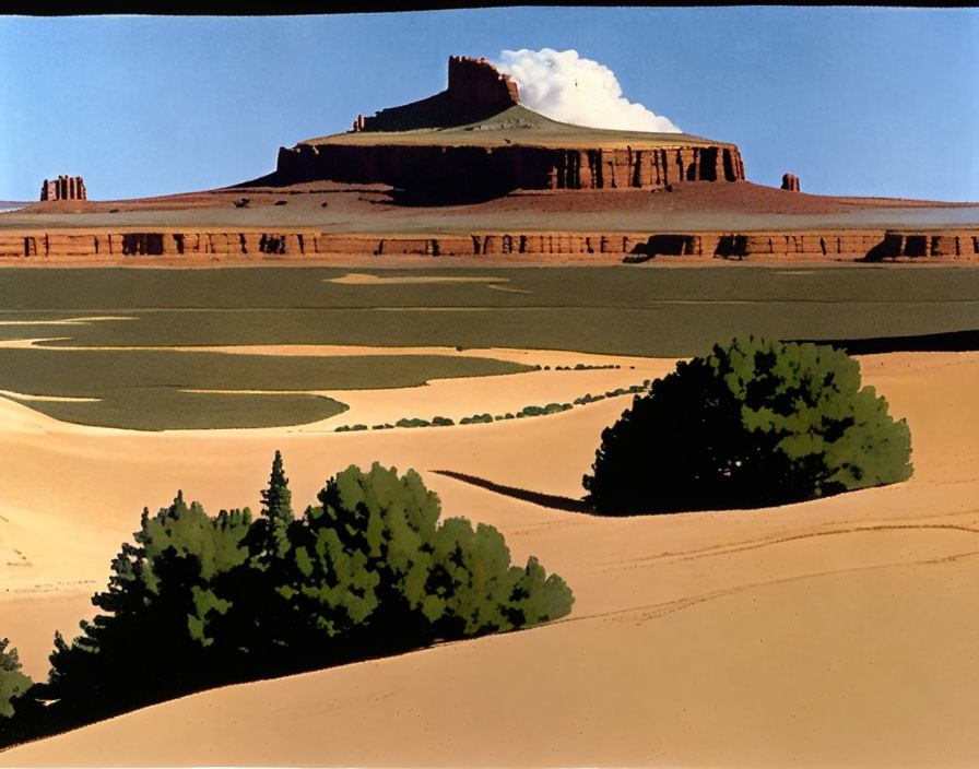 Flat-topped mesa under blue sky with desert sand dunes and greenery.