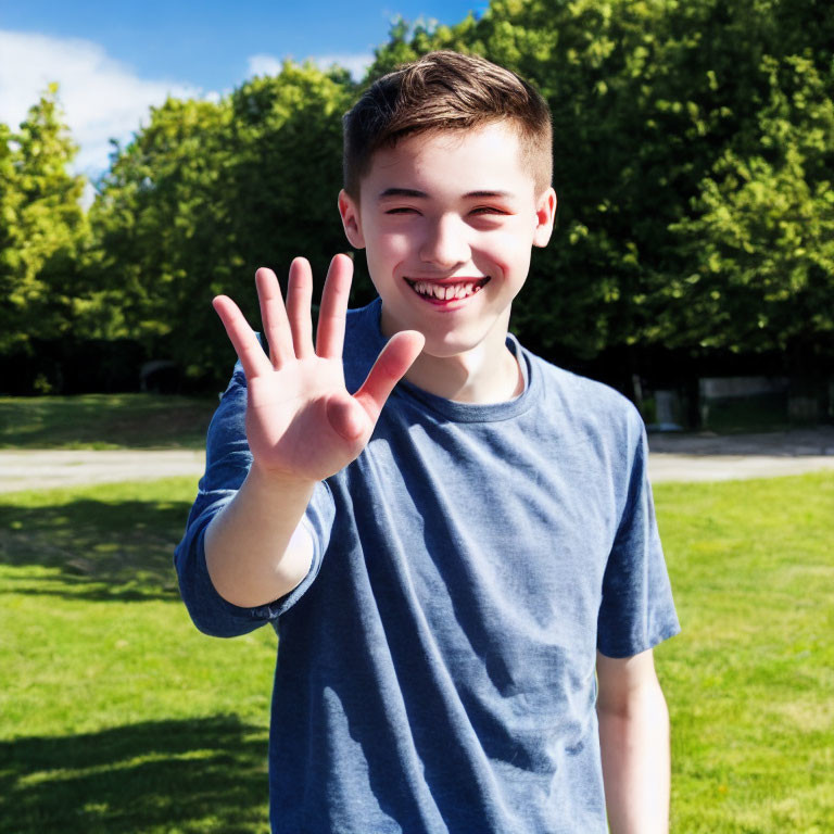 Smiling boy in blue t-shirt waving hand in sunny park