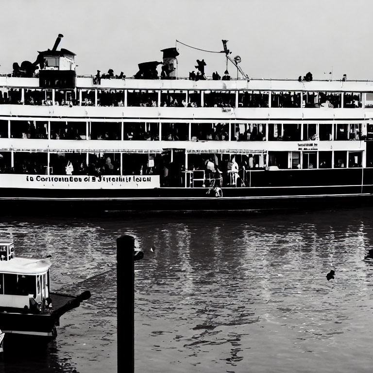 Monochrome photo of multi-deck ferry at pier with passengers and small boat