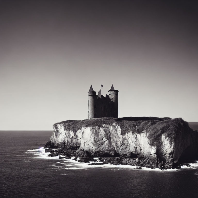 Grayscale image of castle on cliff overlooking calm sea