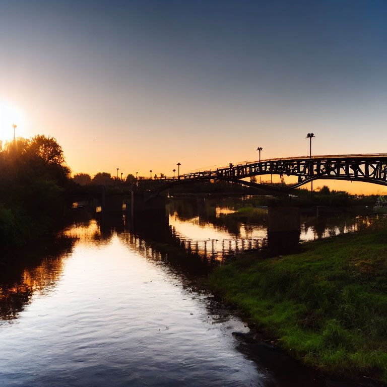 Tranquil sunrise over calm river with pedestrian bridge reflection