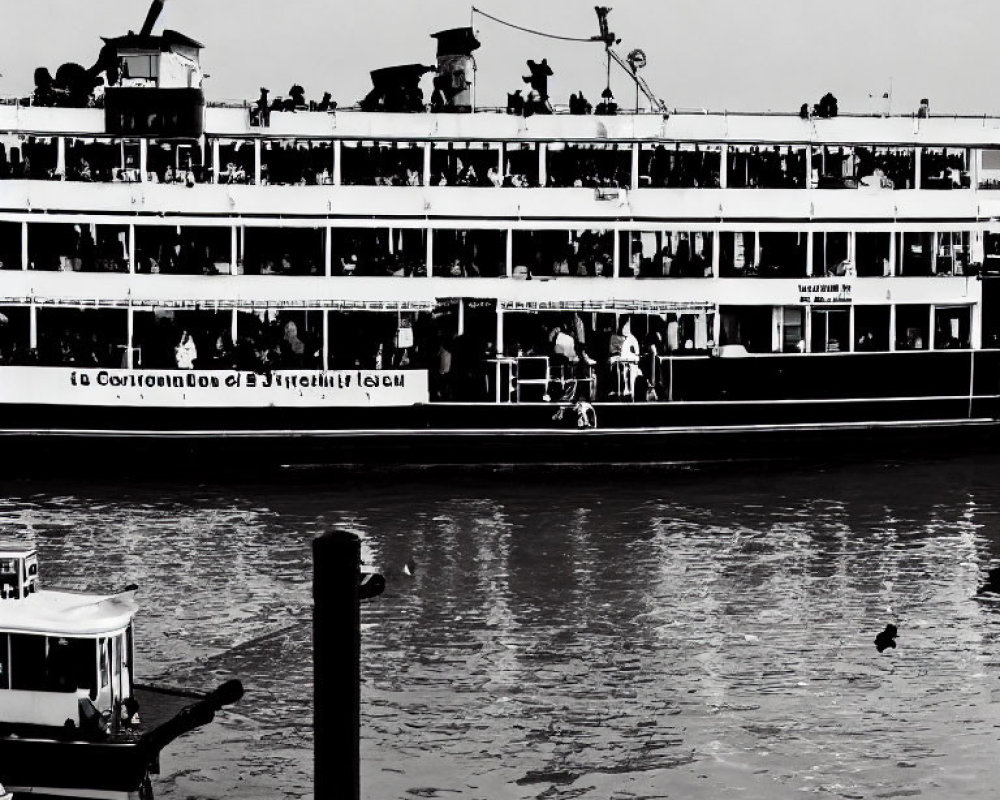 Monochrome photo of multi-deck ferry at pier with passengers and small boat