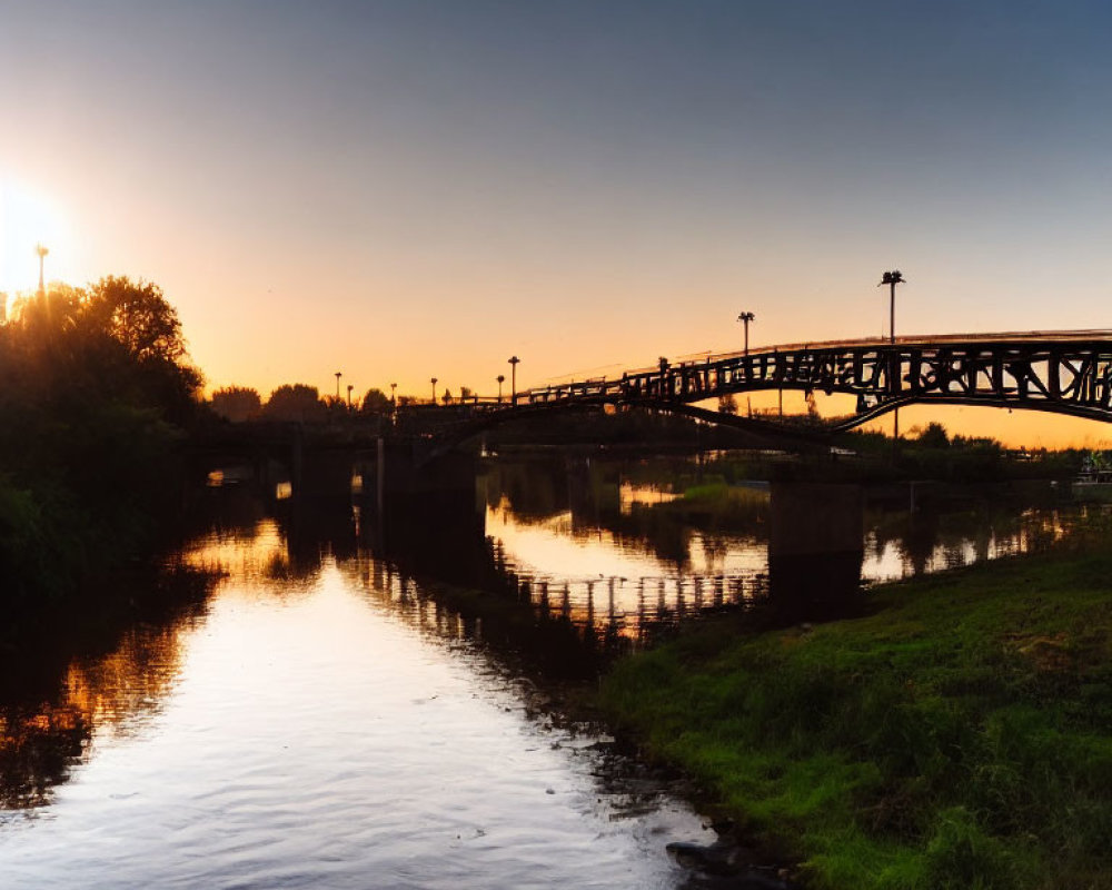 Tranquil sunrise over calm river with pedestrian bridge reflection