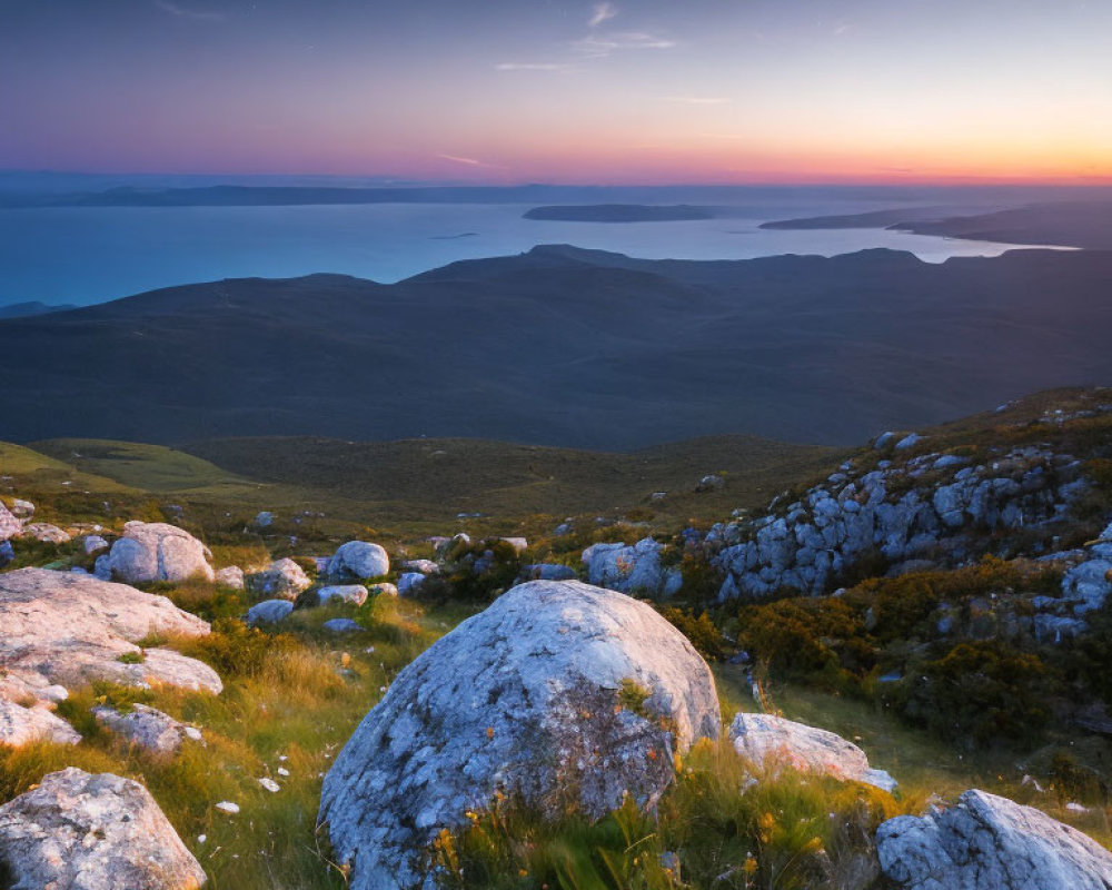 Tranquil landscape with twilight hues, gradient sky, rocks, hills, and calm sea