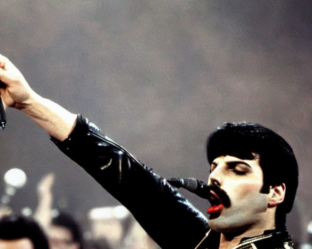 Dynamic concert scene featuring charismatic performer in black leather outfit with microphone and mustache.