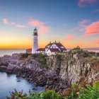 Tranquil sunset scene with white lighthouse on rocky cliff by calm sea