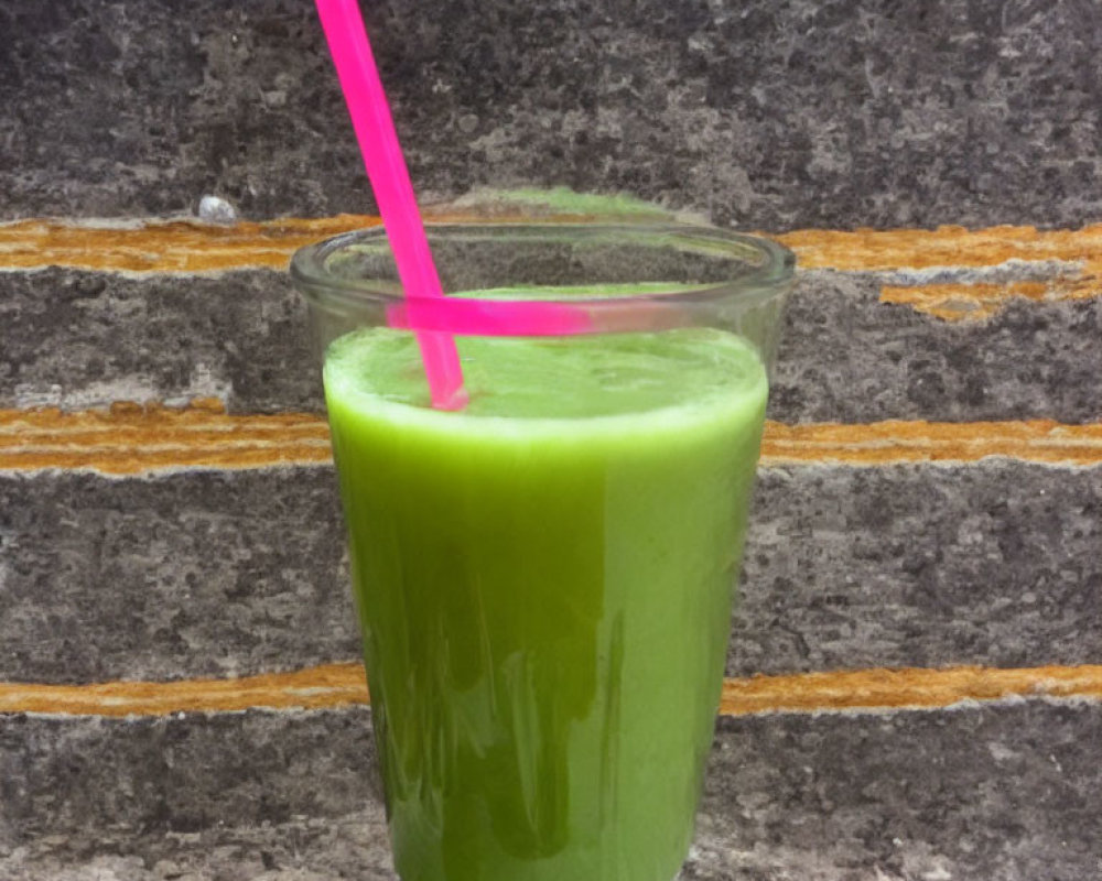 Green smoothie in glass with pink straw against brick wall background