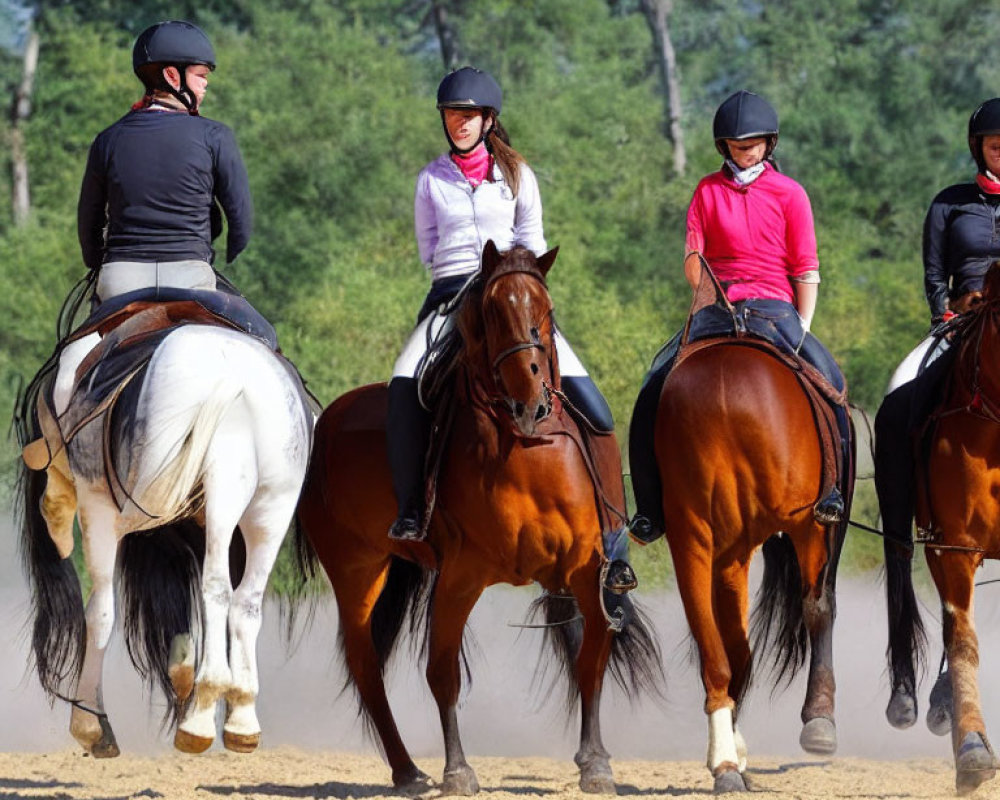 Three equestrians in helmets and riding gear conversing on horses on sandy track.