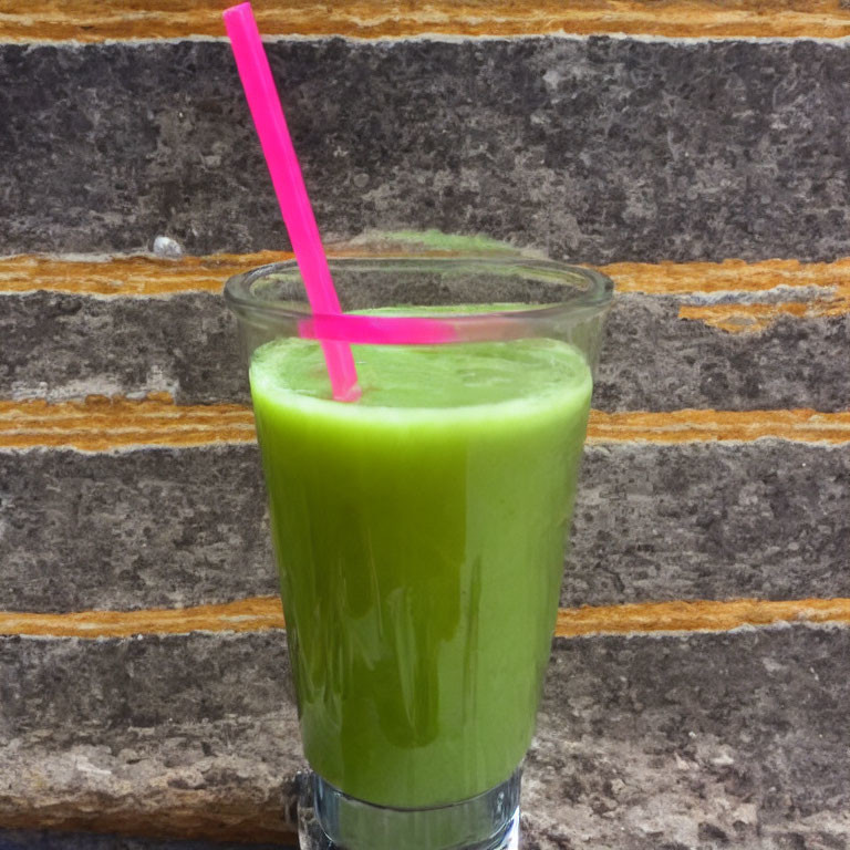 Green smoothie in glass with pink straw against brick wall background