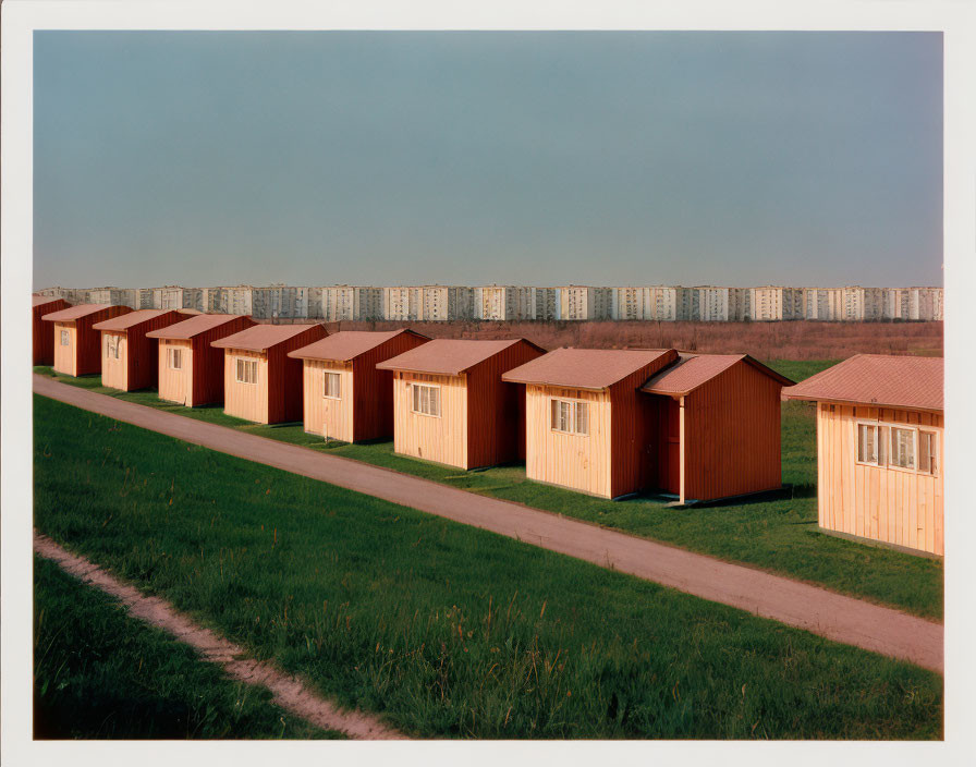 Row of Identical Wooden Huts with Red Roofs Along Grass Path