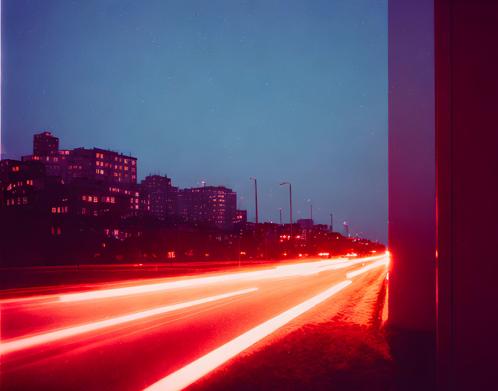 City street at night: blurred vehicle lights, starry sky, buildings.