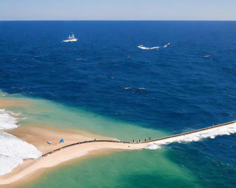 Sandy coastline with jetty, blue sea, waves, boats, and blue parasol.