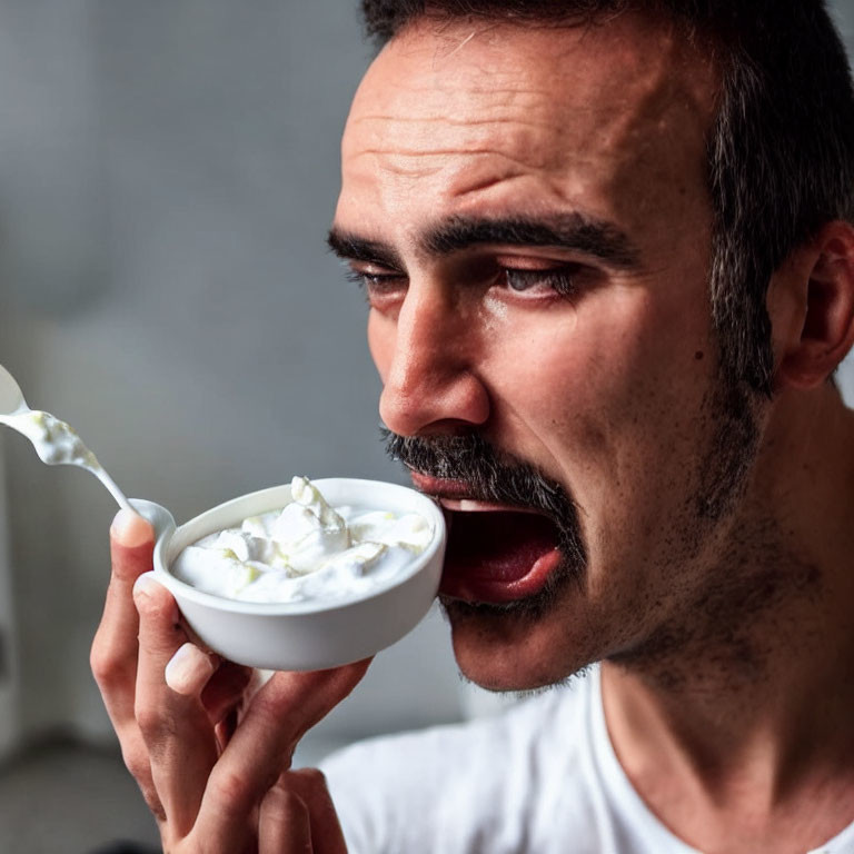 Mustached man eating yogurt with spoon in humorous anticipation