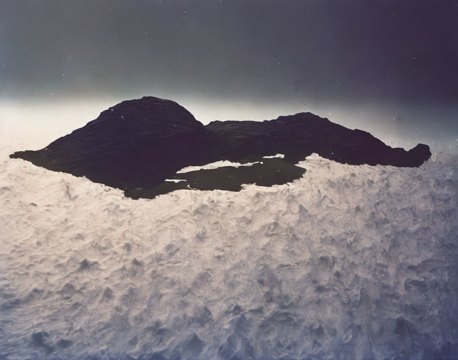 Silhouette of rocky formation against twilight sky with textured foreground.