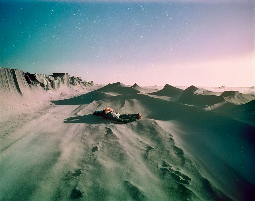 Person lying on sand dunes under twilight sky with visible stars