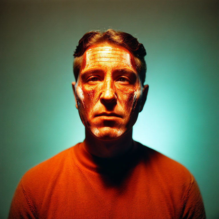 Somber person in orange shirt against teal backdrop with light streaks