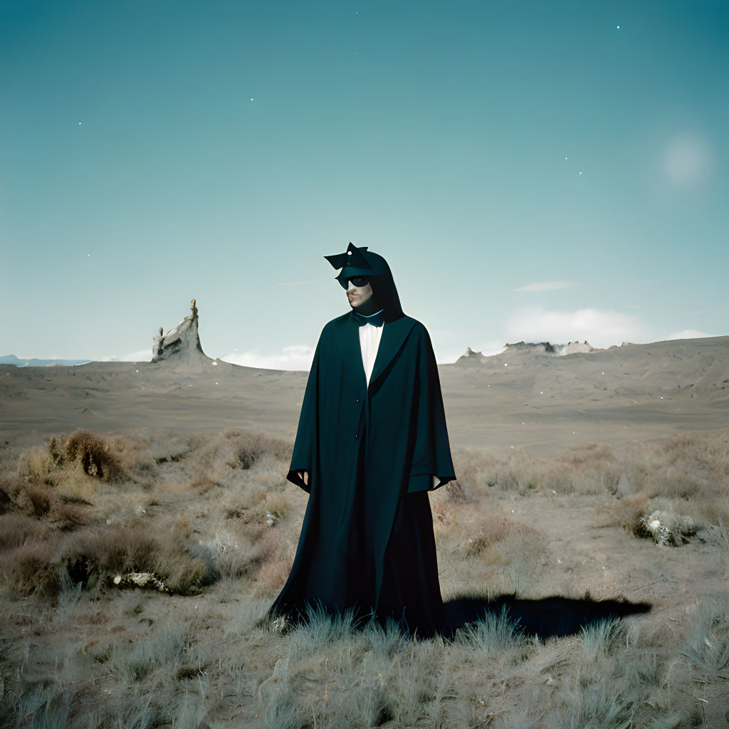 Mysterious figure in dark cloak in twilight desert landscape