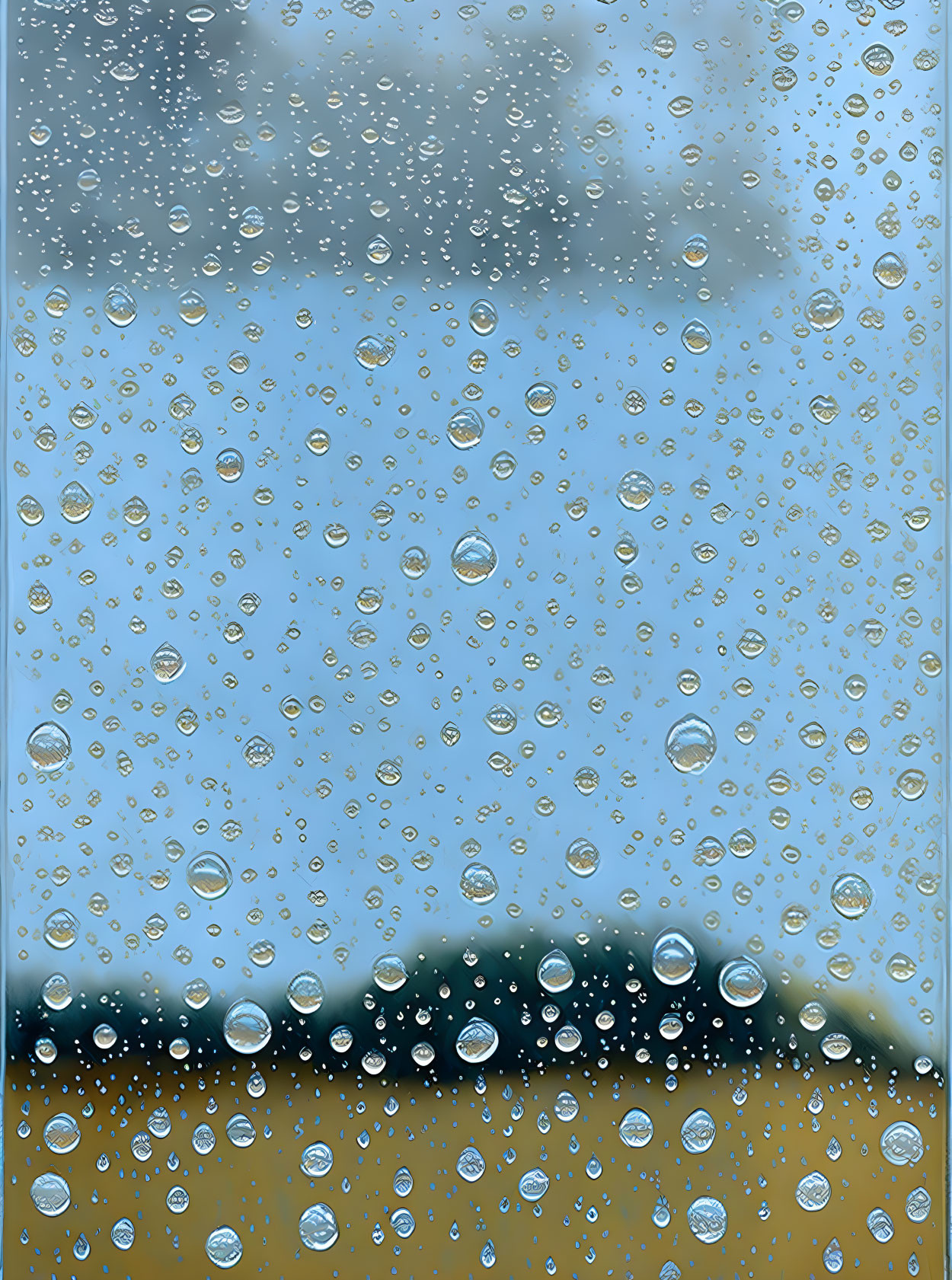 Water beads on glass with blurred sky and greenery background