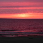 Vibrant pink and red sunset over dark ocean waters